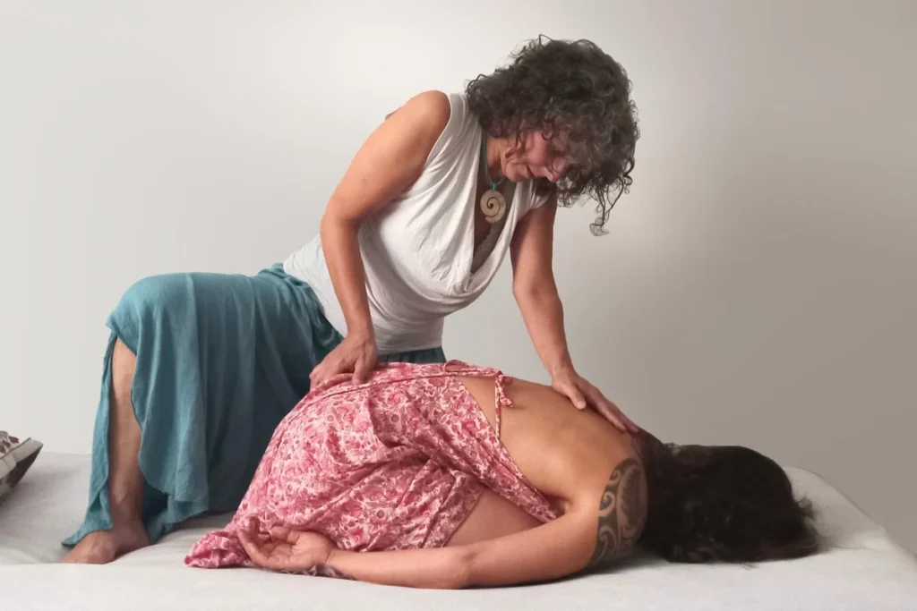Mujer recostada boca a bajo, recibiendo un masaje genital de reconexión.