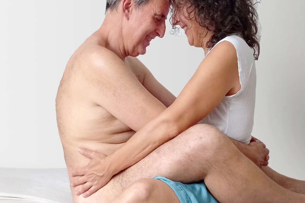 Hombre desnudo abrazado a una terapeuta en una sesión de masaje genital de reconexión.